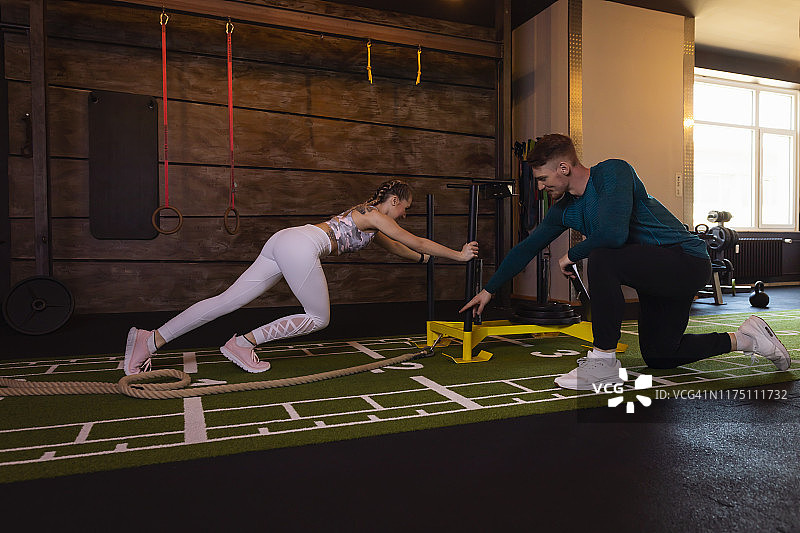 年轻女人在健身房锻炼，私人教练推动负重雪橇图片素材