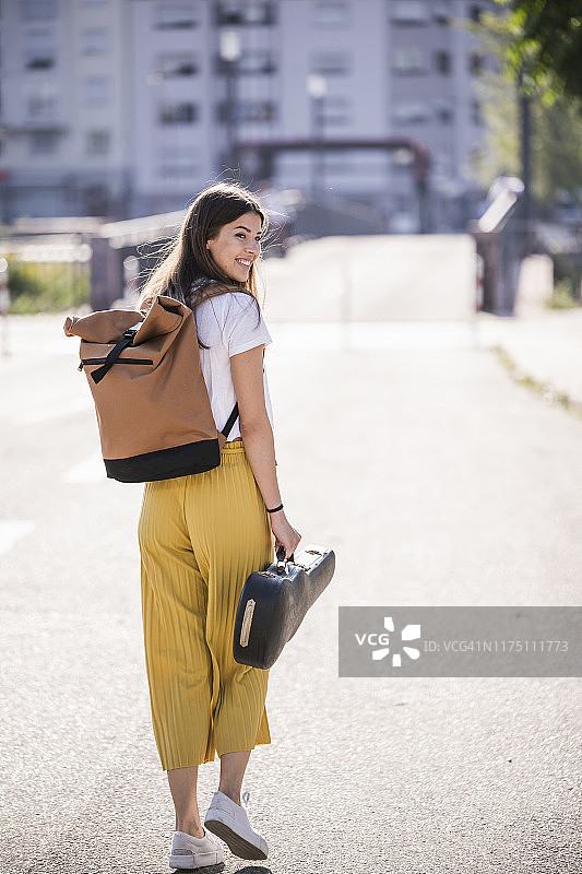 年轻女子提着小提琴琴盒走在街上图片素材