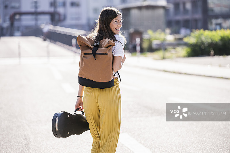 快乐的年轻女人提着小提琴盒走在街上图片素材
