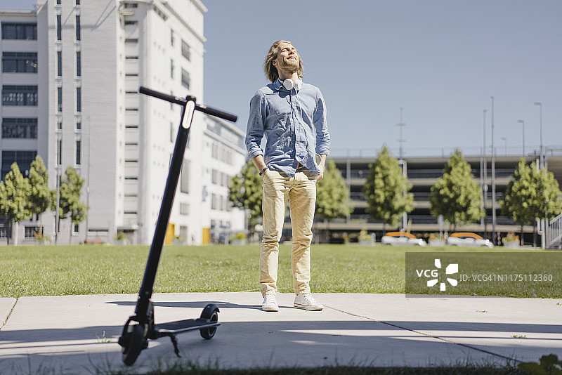 年轻男子站在城市里的电动滑板车旁图片素材