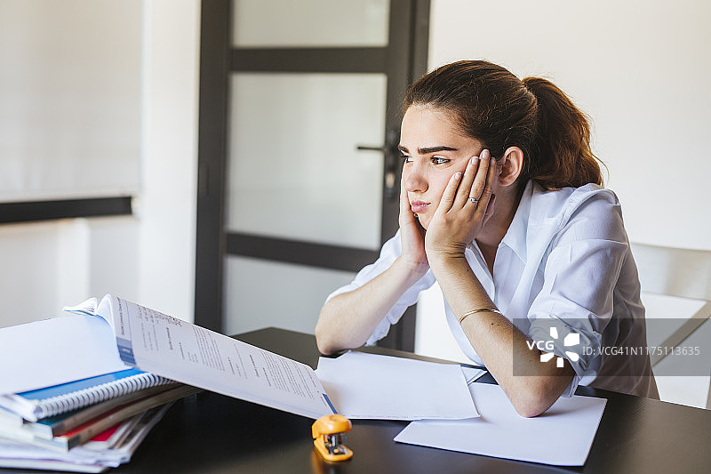 在家中书桌前拿着文件的沮丧女学生图片素材