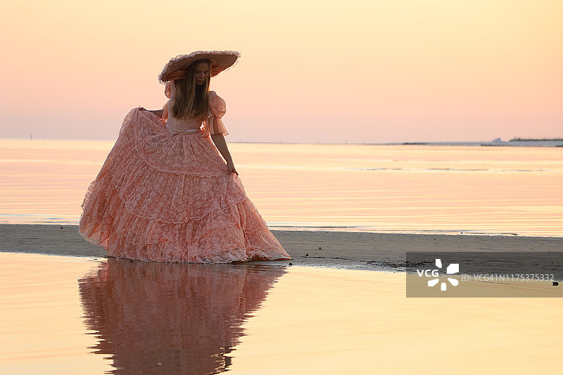 一位女士身穿大型桃色连衣裙，头戴配套帽子，背对阳光图片素材