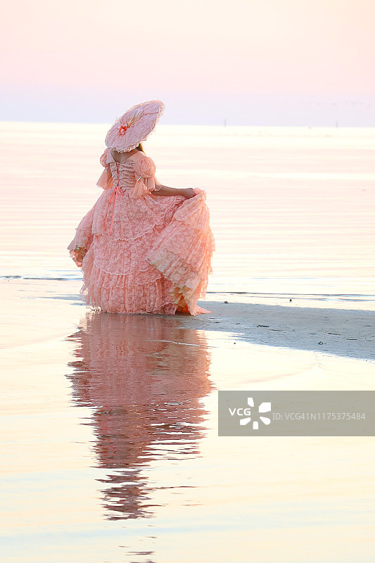 一位女士身穿桃色大礼服，头戴同色帽子，直面阳光图片素材