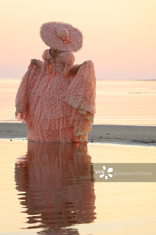 一位女士身穿桃色大礼服，头戴同色帽子，直面阳光图片素材