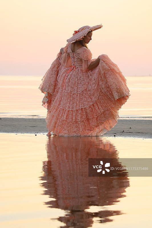 一位女士身穿桃色大礼服，头戴同色帽子，直面阳光图片素材