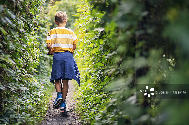 小男孩在栅栏间的小路上骑滑板车图片素材