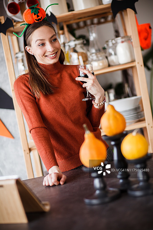 在万圣节厨房里手持葡萄酒的微笑女人图片素材
