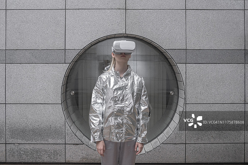 穿着银色套装的女孩在未来城市中戴着VR眼镜观看图片素材