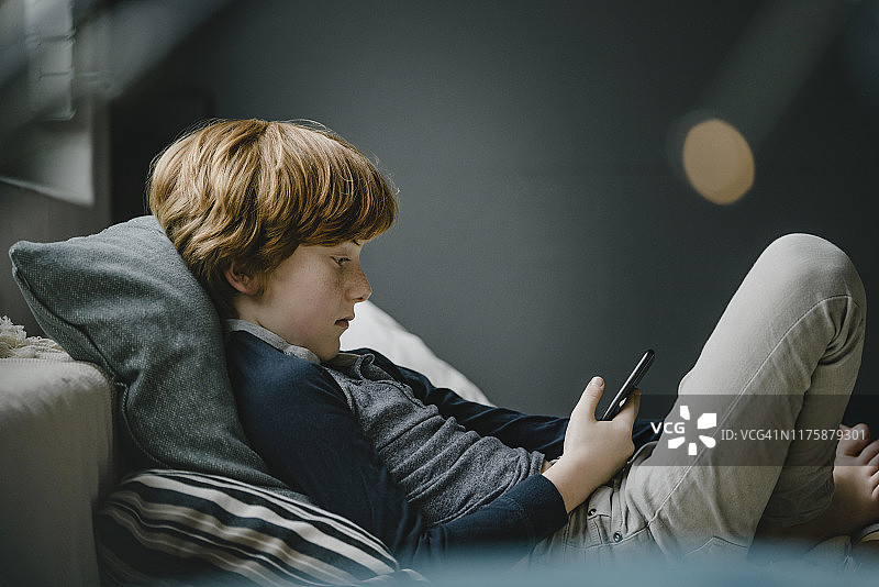 躺在沙发上看手机的红发男孩图片素材