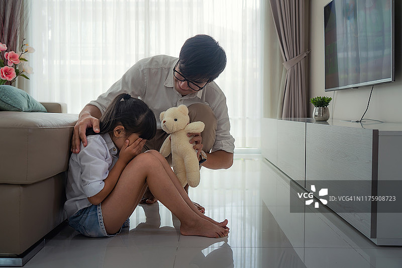 亚洲年轻父亲抱着玩偶，安慰在客厅里沮丧的女儿。家庭生活，爱，关系或挫折，压力和问题概念图片素材