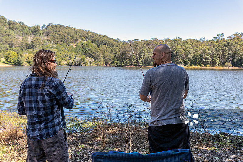 两个快乐的男人在湖边钓鱼时交谈图片素材