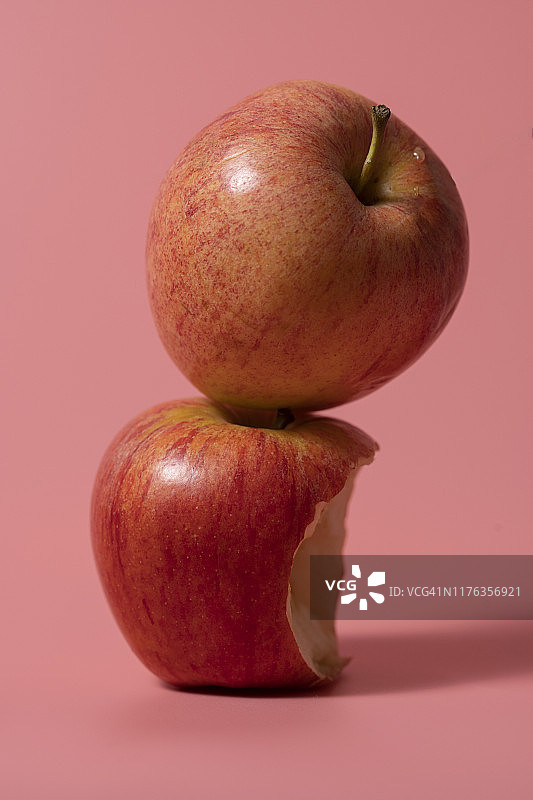 粉色背景上的苹果特写：一个缺了一口，另一个完整图片素材