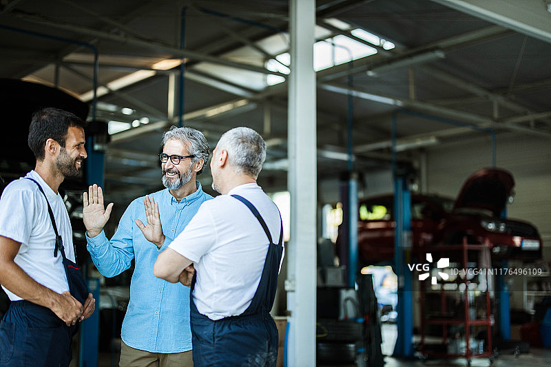 快乐的经理在汽车修理店与机械师交谈图片素材