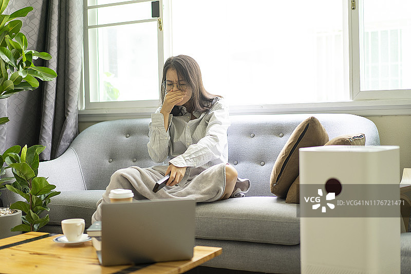 在舒适沙发上咳嗽并感到不适的亚洲女孩图片素材