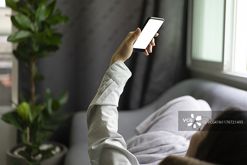 在舒适的沙发上用智能手机与朋友进行视频通话的少女图片素材