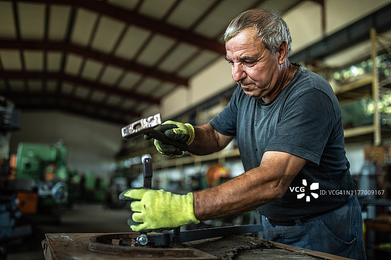 在工厂使用锤子弯曲金属的年长男人图片素材
