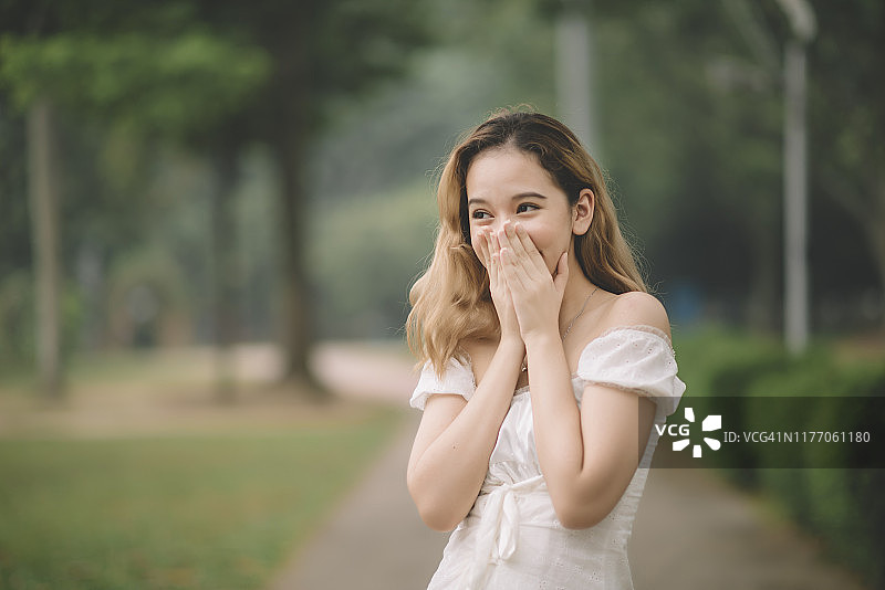 在公园里用手捂住嘴的马来西亚少女图片素材