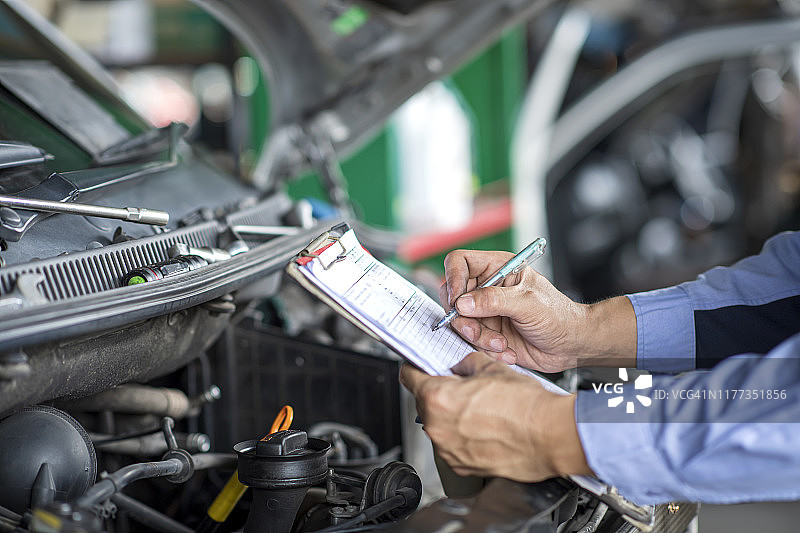 技工在修理厂拿着维修报告的剪贴板。汽车维修服务。图片素材