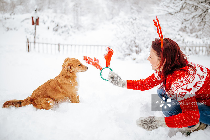 女人和狗戴着驯鹿角享受雪景图片素材