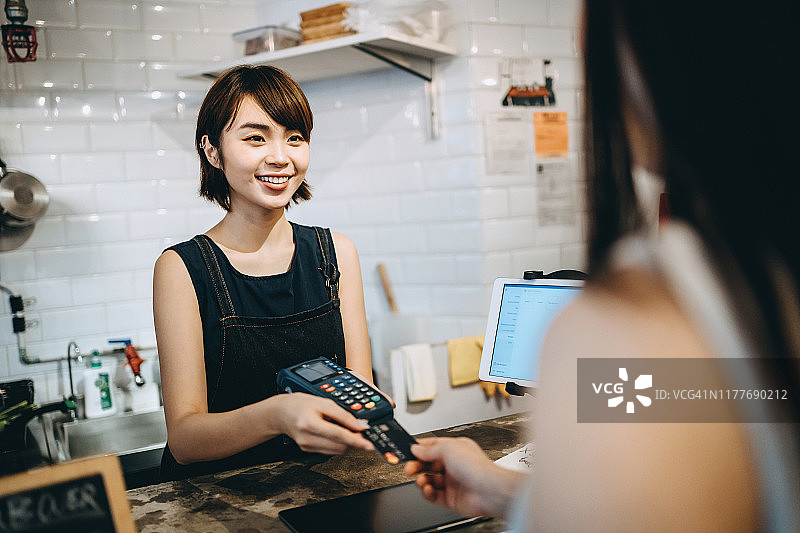 顾客在咖啡馆使用非接触式信用卡快速支付，咖啡师微笑服务图片素材