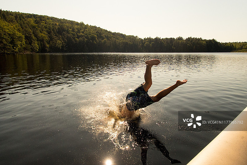 年轻人在湖里头朝下跳水，他的朋友拍照。图片素材