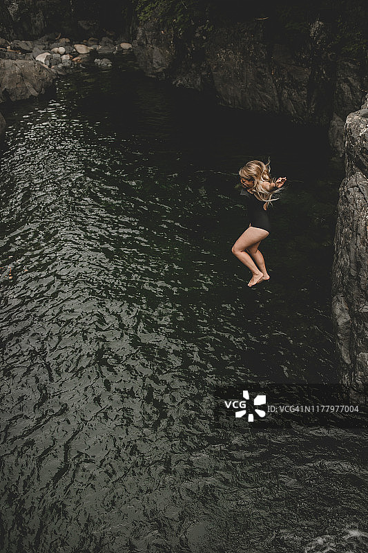 年轻女子悬崖跳入深绿色水中图片素材