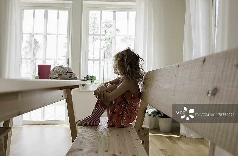 坐在家里的长椅上，抱着腿独自思考的年轻女孩图片素材