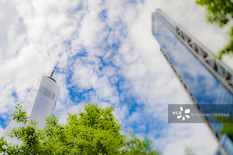 世界贸易中心一号楼和三号楼下的清新绿叶树木，周围环绕着快速移动的卷积云，位于美国纽约州纽约市曼哈顿下城区，拍摄于2019年5月18日图片素材