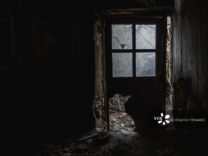 废弃石屋内破损的木制玻璃门，墙壁布满污垢和裂缝，呈现乡村人口减少的概念图片素材
