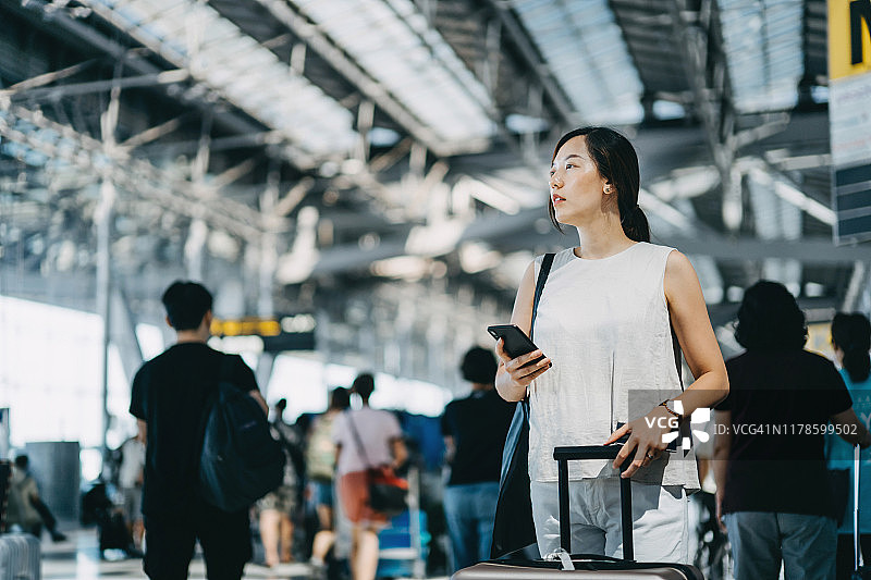 年轻亚洲女性在国际机场大厅使用手机查看信息图片素材