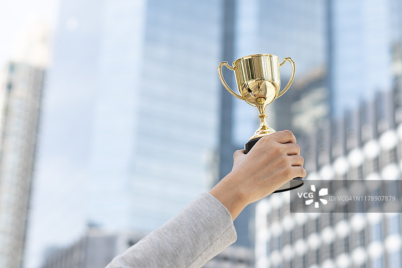 业务目标，商业概念。女商人拿着金色奖杯的特写镜头。图片素材