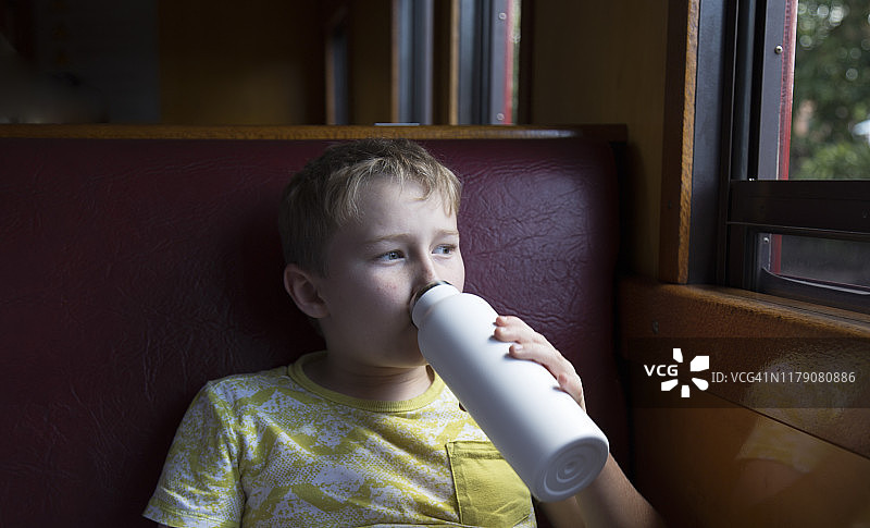 坐在火车上用可重复使用水瓶喝水的男孩图片素材