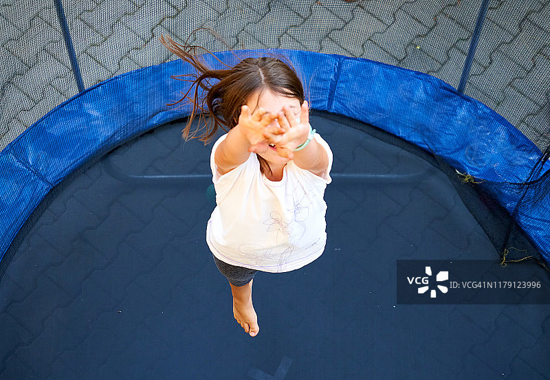 可爱的女孩用手捂着脸在蹦床上跳跃，自然生活方式，罗马尼亚特兰西瓦尼亚图片素材