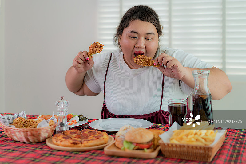 亚洲肥胖女性吃着炸鸡、薯条、汉堡等油炸食品图片素材