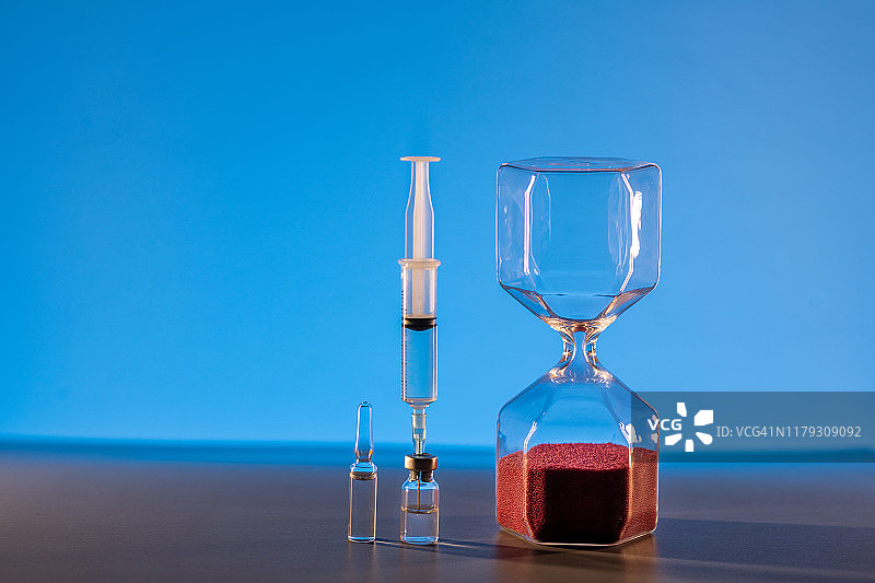 蓝色背景上的沙漏、注射器和药瓶，健康概念图片素材