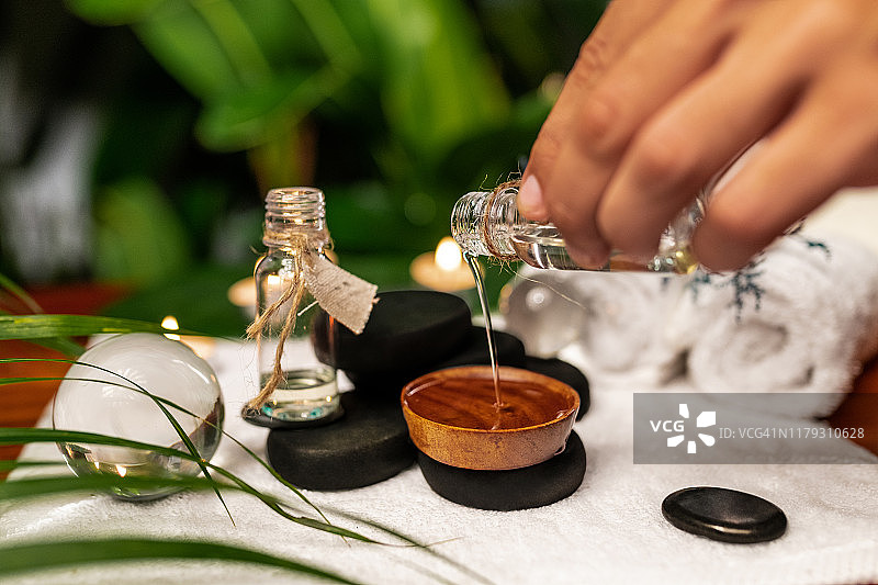 男子将精油倒入石头上的容器中，用于石头疗法，旁边是白色毛巾和薰衣草图片素材