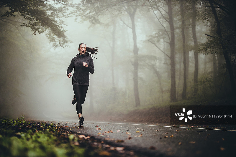 年轻运动型女子在雾林中的道路上慢跑图片素材