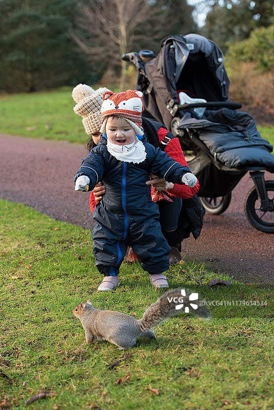 在英国苏格兰爱丁堡的王子街花园，亚洲妈妈和宝宝穿着冬装在棕色松鼠附近玩耍图片素材