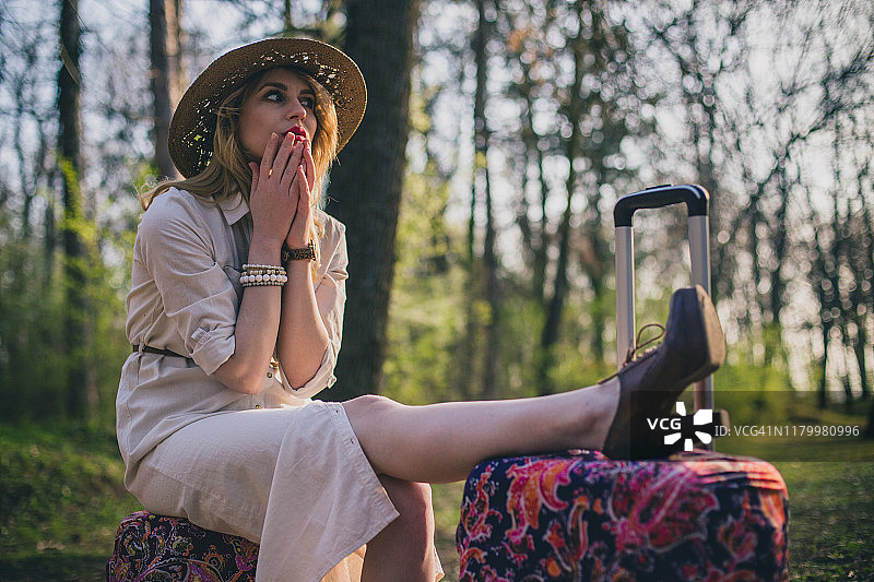 阳光明媚的日子里，年轻女子坐在公园里，身边放着手提箱图片素材