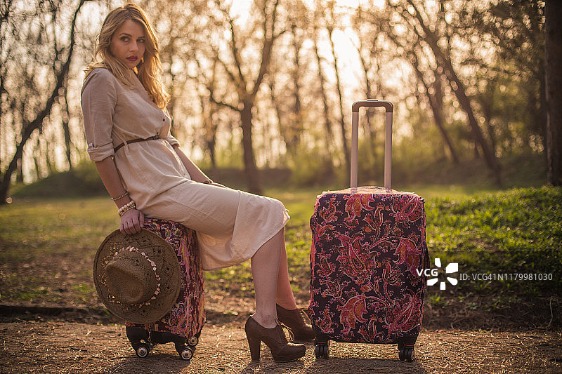 阳光明媚的日子里，公园里带着行李箱的年轻女子图片素材