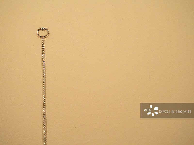 赭色墙壁上，一根钉子上挂着一个带有圆形金属环的链条图片素材