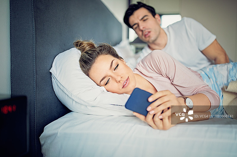 丈夫在床边偷看妻子发短信图片素材