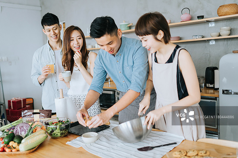 朋友们在厨房里一起准备和烹饪，为聚会聊天，桌子上有各种新鲜蔬菜和食材图片素材