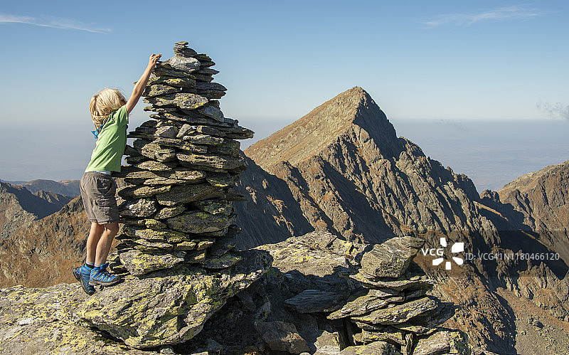 男孩在罗马尼亚法格拉什山脉的科尔努·卡尔图努伊峰堆叠石头，背景是尼戈尤峰图片素材