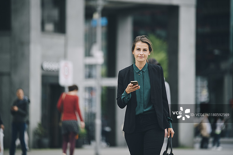 在城市街道上拿着智能手机行走的自信女商人画像图片素材
