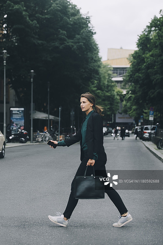 商务女性在城市街道上过马路的侧面视角图片素材