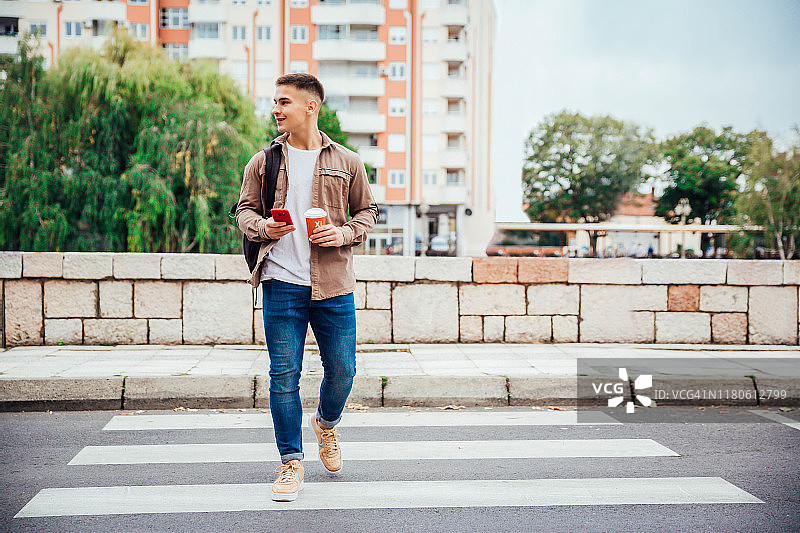 年轻男人穿过街道使用手机图片素材
