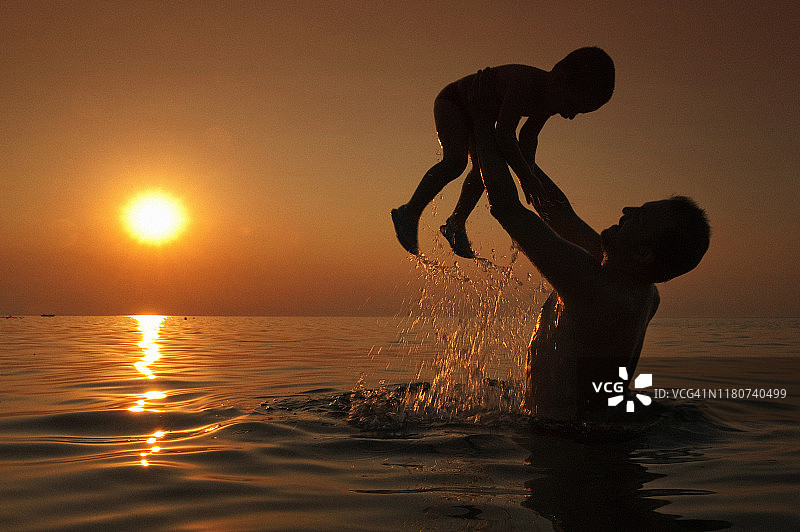 父亲高举小儿子夕阳逆光图片素材