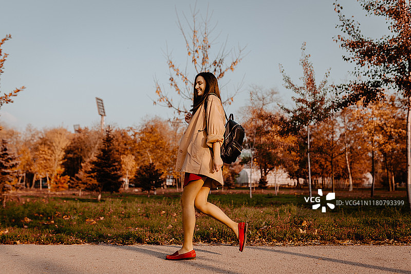 在阳光明媚的秋日，年轻女人在公园里散步图片素材
