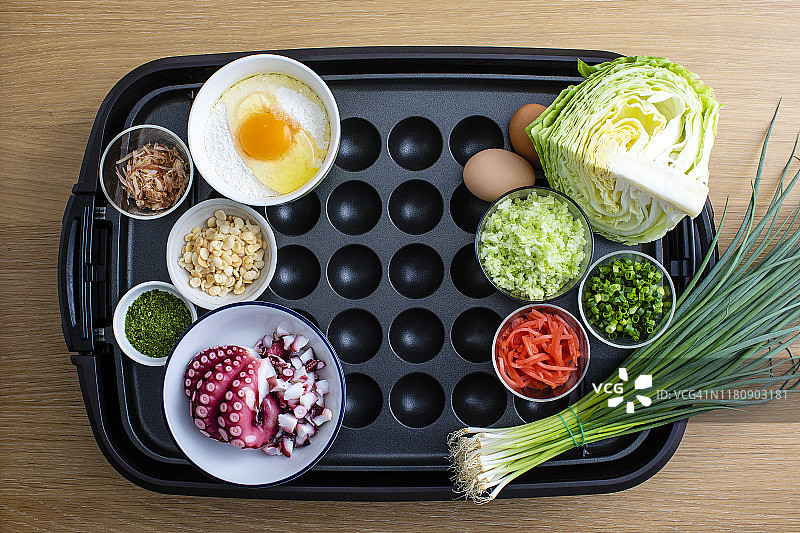 烤章鱼食谱，铁板上放置章鱼、韭菜、鸡蛋、面粉、卷心菜和鲣鱼等食材，从上方拍摄图片素材